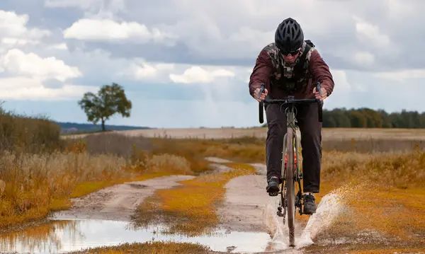 Mountain biker riding a gravel bike through a muddy puddle leaving splashes of water in the field