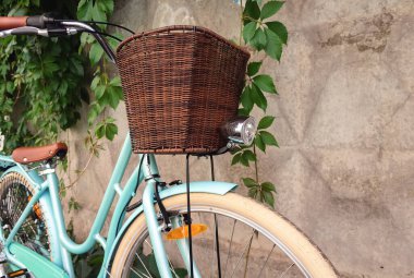 Hasır sepetli ve farlı klasik bisiklet yeşil bitkilerle beton bir çitin yanında duruyor..