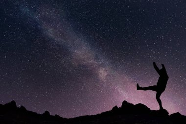 Yıldızlı gökyüzünde Samanyolu ile gece manzarası ve dağın tepesinde mutlu bir kız.