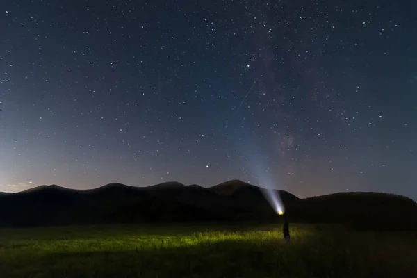 Dağların üzerinden yıldızlı gece gökyüzü ve fenerli bir adam. Doğal manzara..