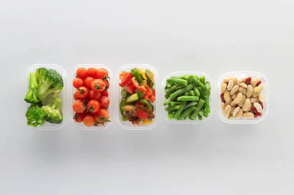 Frozen vegetables in plastic containers on white background. Frozen broccoli, green beans, cherry tomatoes, beans and bell pepper.