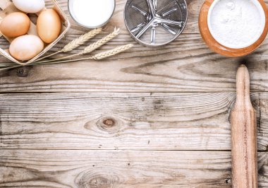 Ahşap mutfak atölyesinin üst manzarası. Masanın üzerinde bir sepet yumurta, bir bardak süt, bir elek bardağı, bir merdane ve bir tencere un var..