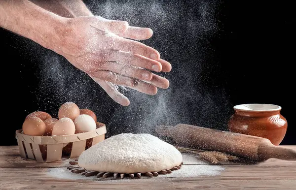 The baker claps his hands with flour over the dough. A man is preparing homemade bread in the kitchen. The concept of home comfort. Healthy food.