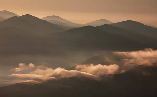 Beautiful mountain landscape with low clouds, rays of light through the mountain peaks and morning fog at dawn.