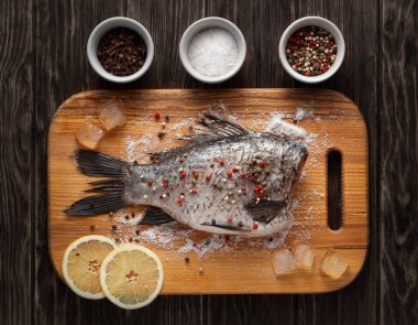 Crucian sazanı ahşap mutfak tahtasında biber, tuz ve limonla pişirmeye hazır..