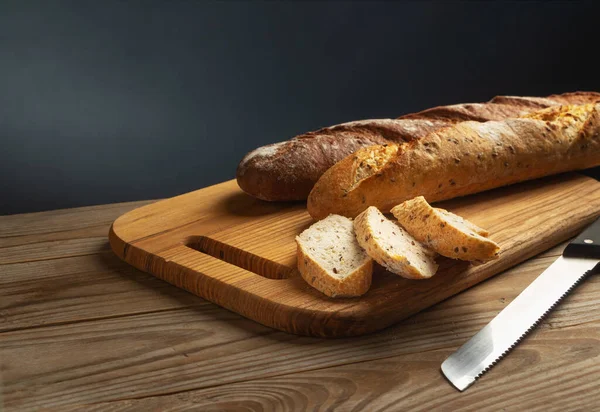 Freshly baked baguettes on a cutting board with chopped pieces on grey background.