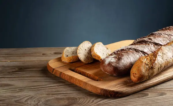 Freshly baked baguettes on a cutting board with chopped pieces on grey background.