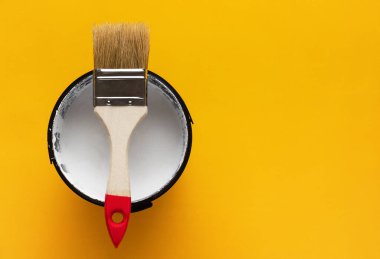 Teneke kutunun üstüne boya fırçası ve sarı arka planda beyaz boya. Yenileme konsepti.