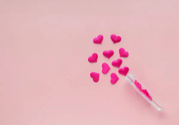 Fabric hearts from a test tube on a pink background.