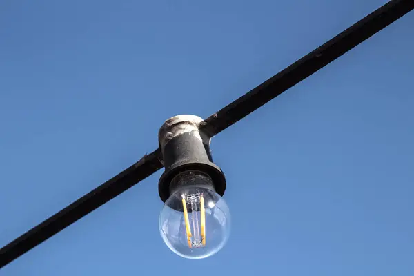 stock image Incandescent bulb on a black wire against the sky