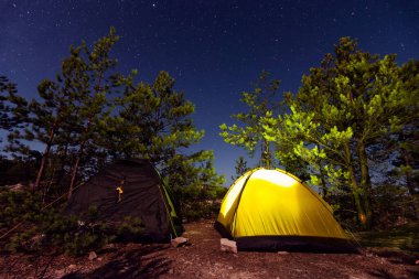 İçinde yanan bir ışık bulunan iki çadır yıldızlı gökyüzünün arka planında. Çadır şehrin güzel manzarası parlak yıldızlarda mavi gökyüzüne karşı. Turizm ve açık hava aktiviteleri kavramı.