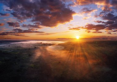 Hava manzarasından gün batımında sisli tarlaların üzerinde dramatik gökyüzü olan renkli bir sabah manzarası..