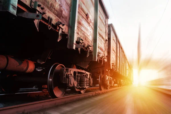 Freight train passing at sunset. Train carrying cargo under the rays of the setting sun.