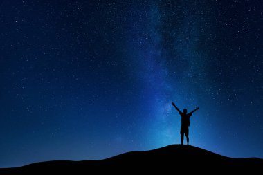 Bulutlu gökyüzünde Samanyolu 'nun güzel gece manzarası ve elleri havada genç bir adamın silueti. Zafer ve başarı kavramı.