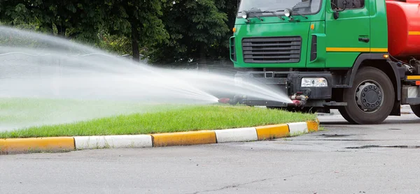 A truck for watering the lawn pours water on the lawn with water jets. City lawn care services.