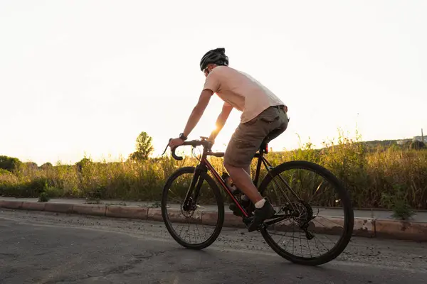 Młody Sportowiec Kasku Jeździ Żwirowym Rowerze Asfaltowej Drodze Zachodzie Słońca — Zdjęcie stockowe