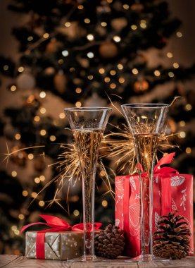 Noel hediyeli iki kadeh şampanya ve arkaplanda yanan kıvılcımlar..