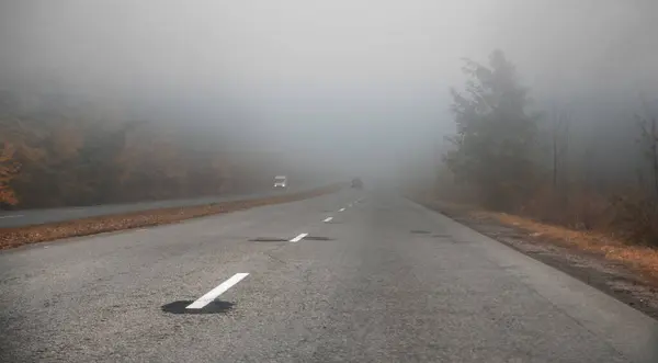 Departing road into a foggy cloud. On the road, cars go through the fog. Demonstration of poor visibility on the road.