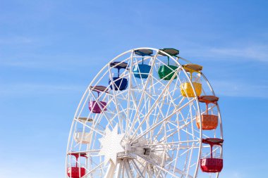 Mavi gökyüzünün arka planında çok renkli taksileri olan dönme dolap.