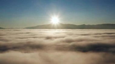 Gün doğumunda yoğun bulutlar ve sislerle dolu resimli bir dağ manzarası. İnsansız hava aracı bulutlara doğru uçuyor.