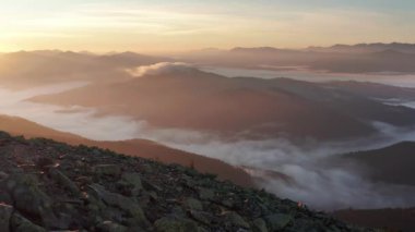 Genç kız dağların zirvesinde duruyor ve güneşin doğuşunu izliyor. Sabah sisi, kayalar ve vadide dramatik güneş ışığı olan dağ manzarası. Hava aracı görünümü.