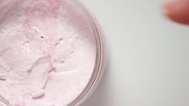 Kadın pembe el kremini parmağıyla kavanozdan alıyor. Üst görünüm.