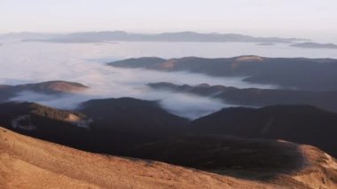 Dağ yamacı, alçak bulutlarda bir dağ vadisinin arka planına karşı havadan bakıldığında gün doğumunda. Güzel eğim drone atışını gösterir.