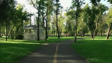 Bir yaz günü yeşil çimenler, çardaklar ve ağaçlarla parkta yürüyüş yolu boyunca yürü. Pürüzsüz İHA uçuşu,