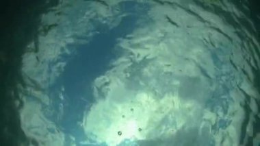 Suyun altından çıkan ve bulutlu mavi gökyüzüne bakan kamera. Su altı el kamerası görüntüleri.