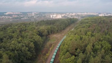 Yük treni, hava aracı görüntüsünden yeşil ormanın içinden şehre gidiyor..