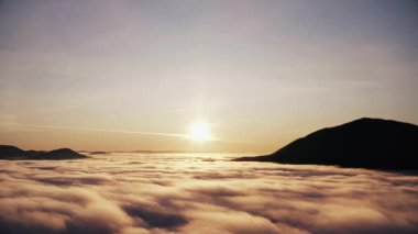 Alçak bulutlu dağlarda güzel bir gün doğumu manzarası. Sabah sisinin dramatik manzarası, bulutlardan sarkan dağ tepeleri, şafakta güneş..