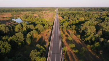 Gün doğarken nehirden geçen arabalarla nehir üzerindeki yol köprüsünün havadan görüntüsü..