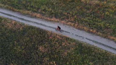 Bisikletlinin altın saatinde virajlı toprak bir yolda hızla giderken hava manzarası. İHA görüntüsü. Etkin yaşam tarzı kavramı.