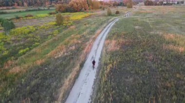 Gün batımında toprak bir yolda bisiklet süren bir bisikletçi. İHA görüntüsü. Etkin yaşam tarzı kavramı.