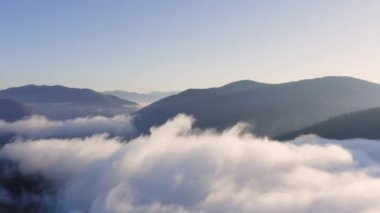 Gün batımında bir dağ vadisinde kabarık bulutlarda İHA uçuşu. Dağların tepelerinde alçak bulutlar ve güneş ışınlarıyla kaplı bir vadide inanılmaz doğal manzara..