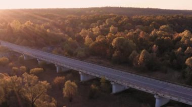 Kamyon güneş doğarken sonbahar ormanındaki köprü boyunca gider. Hava görüntüsü. Lojistik, dağıtım ve ulaşım kavramı.