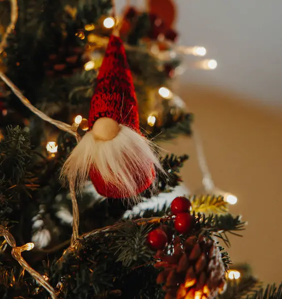 Gnome ornament with a big nose, white beard, and a red hat on a christmas tree with soft white string lights