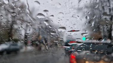 Erimiş kar ve yağmur damlaları arabanın ön camına düşer. Açık hava bulanık, kış mevsimi yağmuru araç penceresinden görülebiliyor.