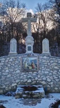 Sacred fountain at Hancu Monastery in Republic of Moldova. Winter snowy view of a cold water spring flowing out of stone decorated with Jesus icon and Holy Cross