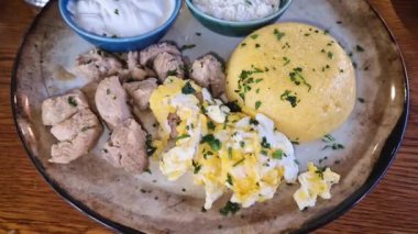 Traditional Moldovan food, meal closeup with pork stew, mamaliga polenta, fried eggs, cheese and sour cream sprinkled with parsley