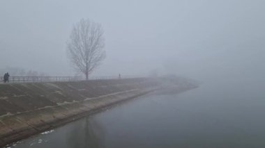 Dense mist in the morning near the lake, with people crossing the dam throughout the thick fog