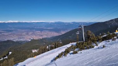 Pirin Dağları 'ndaki Bansko kayak merkezi. Sandalyeleri karlı yamaçların üzerinden geçiyor ve tepeden eski kasabaya doğru güzel bir manzara var.