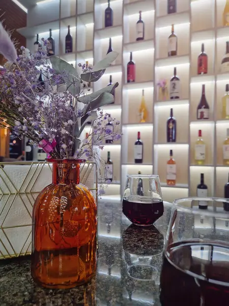 Fancy restaurant interior view, flower vase on the table with wine glasses and shelves with bottles on the background