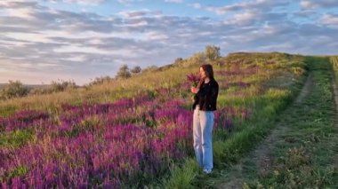 Doğayla uyum içinde genç bir kadın, mor bir Salvia nemorosa çayırının ortasında bir buket Balkan cetveli, yabani adaçayı kokusu alıyor. Mutlu dişi vahşi doğada kendini özgür hissediyor.