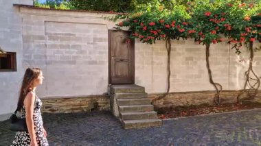 Genç bir kadın güzel bir avluda yürüyor, güneşli bir yaz gününün tadını çıkarıyor, evin duvarlarında turuncu sarmaşıklar, trompetler, çiçekler...)