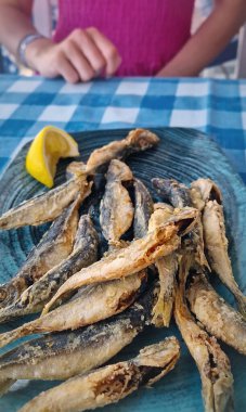 Lokantada masada kızarmış at uskumrusu tabağı ve yukarıda limon suyu sıkan bir kadın, yemeğin tadını çıkarmaya hazır.