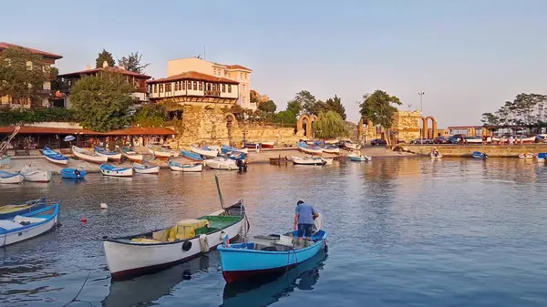 Gün batımının ılık ışığında sakin bir liman sahnesi, çok sayıda küçük tekne sakin sularda yüzüyor. Bulgaristan 'ın Nessebar kentinin geleneksel tarihi binaları ve antik kalıntıları, UNESCO dünya mirası