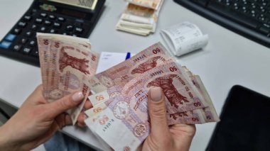 UNGHENI, MOLDOVA - 18 ARALIK 2024 Kadın muhasebeci hesap makinesi kullanarak masanın üstündeki paraları sayıyor. Bir yığın Moldova 50 Lei banknotları. Finansal hesaplamalar veya nakit işleme