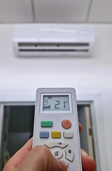 Yakından bakan adam klima sistemine uzaktan kumanda tutuyor alçak düğmeye basarak odadaki sıcaklığı rahat bir seviyeye ayarlamaya çalışıyor. Sıcak mevsimlerde ev serinliyor