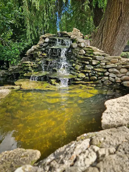 Yosun kaplı taşların üzerine dökülen şelalelerle kristal berrak bir gölete atılmış bozuk paralarla zarif bir bahar. Altın güneş, dalgalanan suyun üzerinde dans eder. Huzurlu sahne doğal güzelliği yansıtıyor.